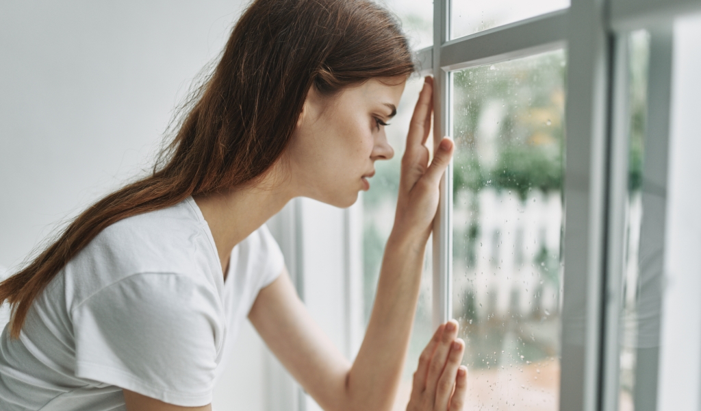 Eine junge Frau schaut traurig aus einem Fenster.